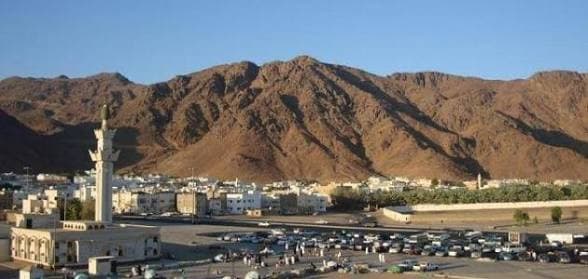 White mosque and minaret in a town at the base of rugged brown mountains.