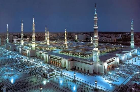 Illuminated Prophet's Mosque in Medina at night with multiple tall minarets and glowing courtyards.